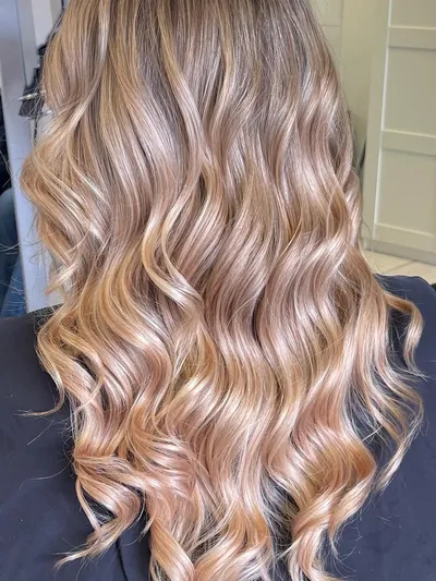 Back view of long curled hair with rooted balayage fading into warm caramel-blonde ends